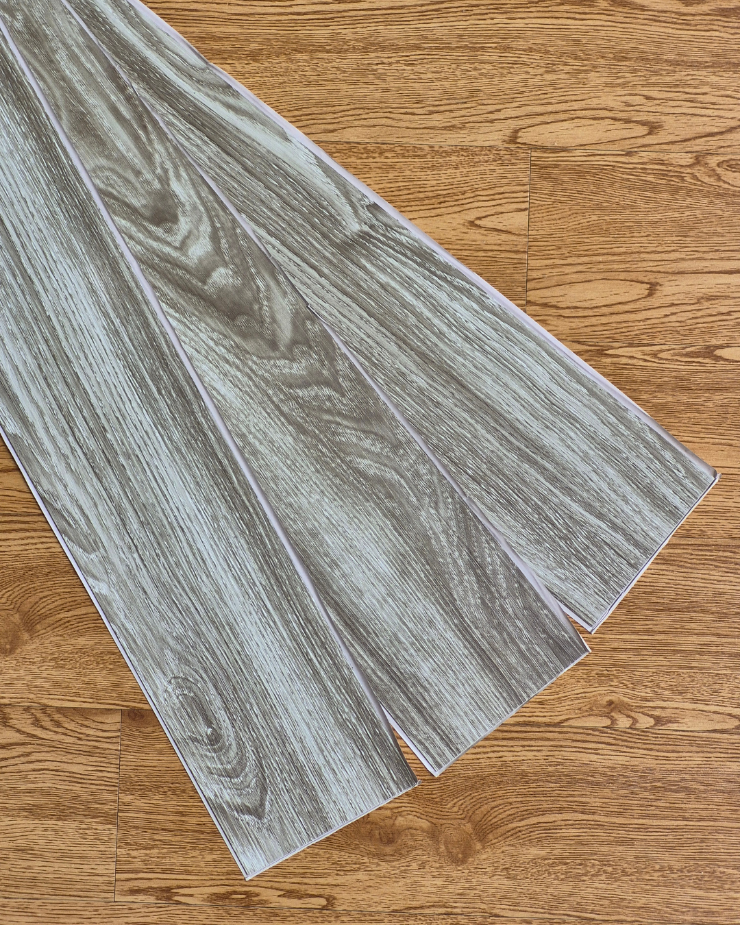 Sheet of gray wood-patterned vinyl flooring on a wooden floor.