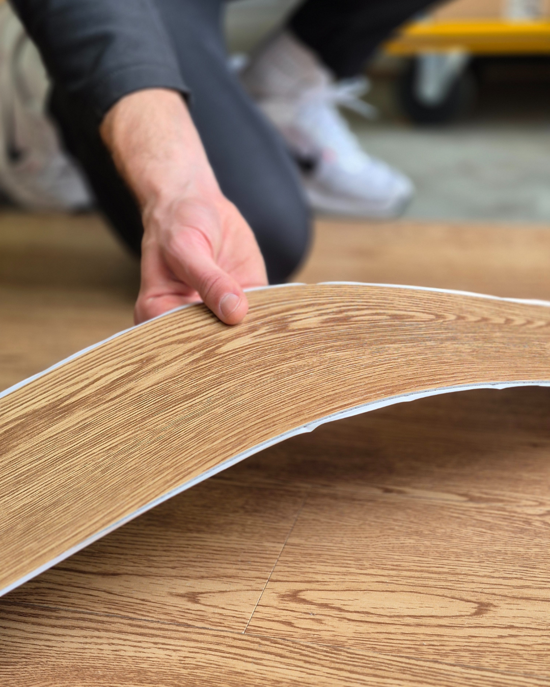 Person holding a sheet of wooden-patterned vinyl flooring