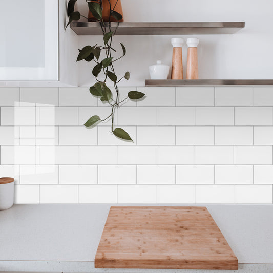 Kitchen with white tiled wall, wooden cutting board, and shelves with decor items.