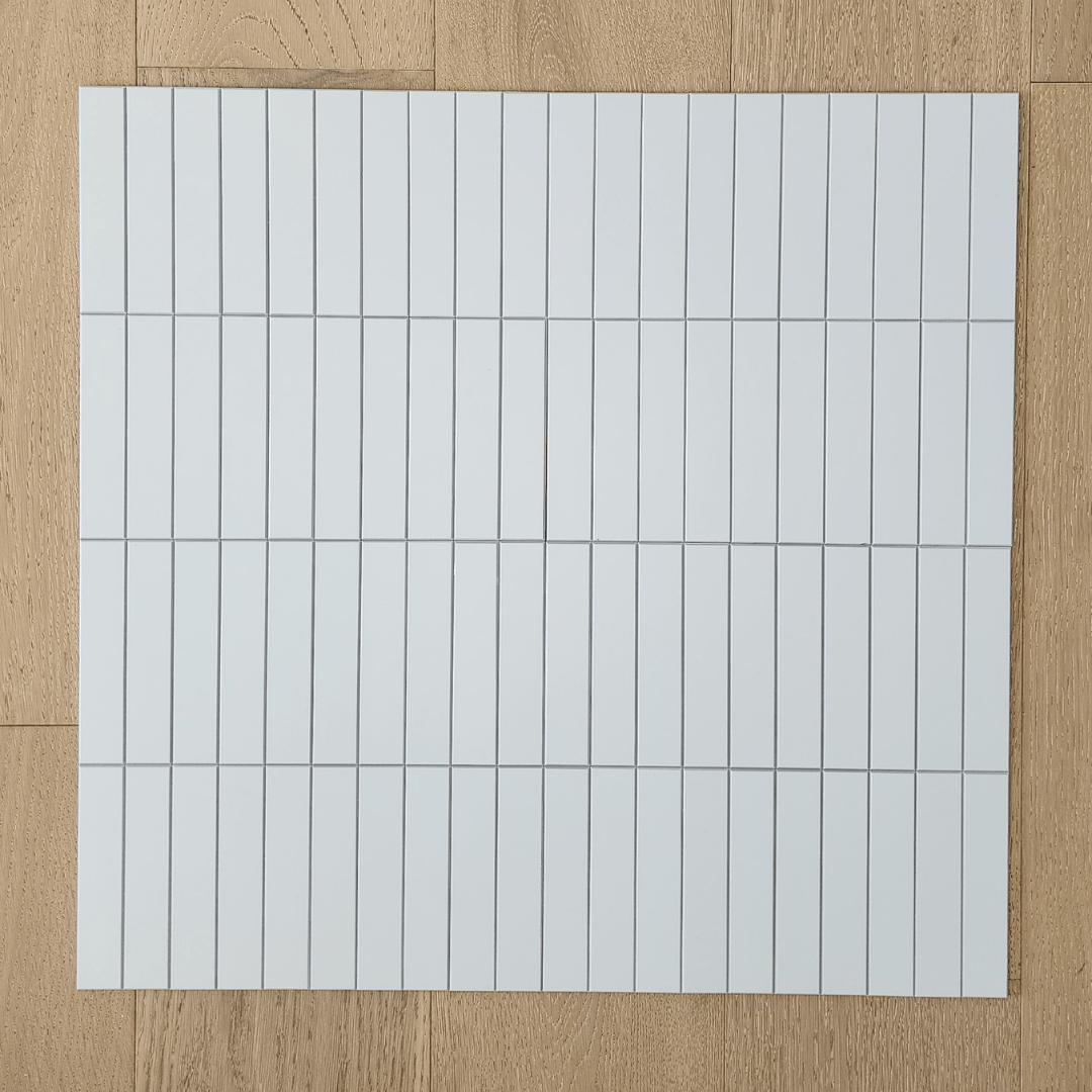 Kit Kat Stick on Composite Tile in Matte White laid on a wooden floor, displaying its grid pattern and clean, modern aesthetic.