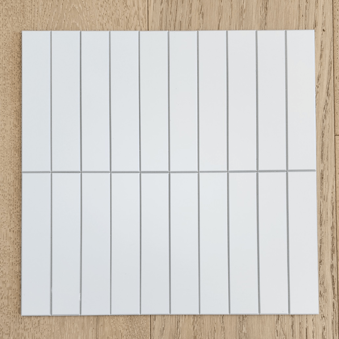Kit Kat Stick on Composite Tile in Matte White placed on a wooden surface, showcasing its sleek and easy-to-install design.