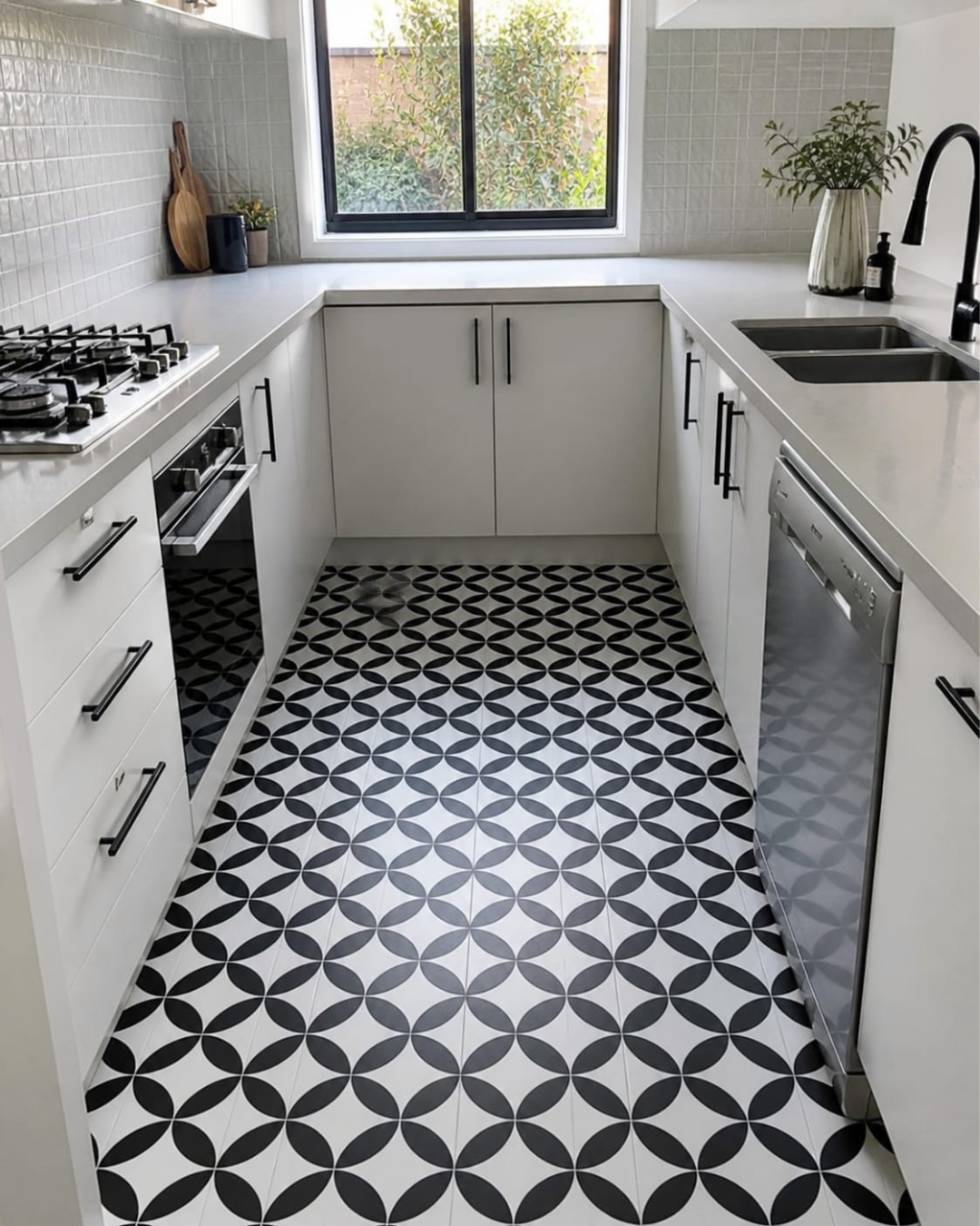 Modern kitchen with white cabinets, black and white patterned floor, and window view.