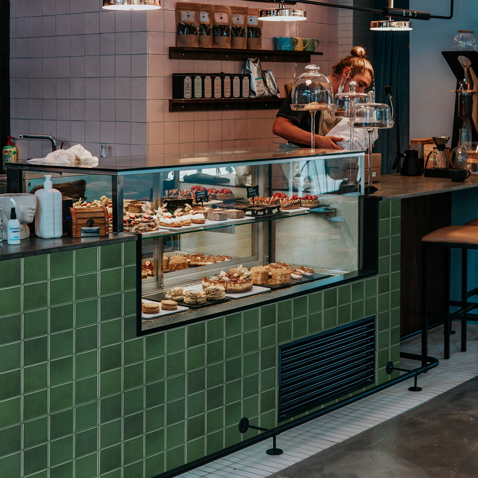 Green tiled pastry case with various pastries in a cafe setting