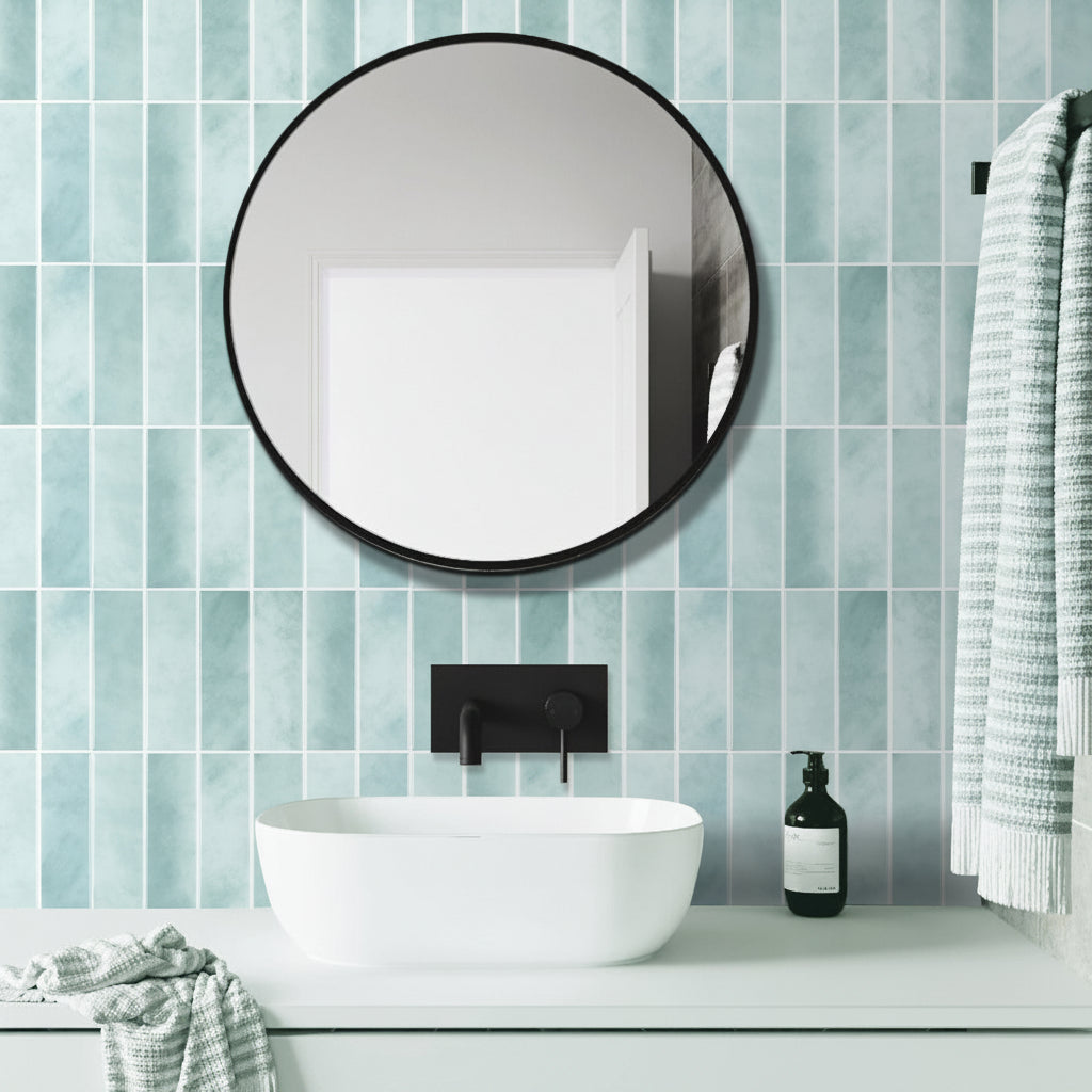Bathroom with round mirror, white sink, and blue tiled wall.