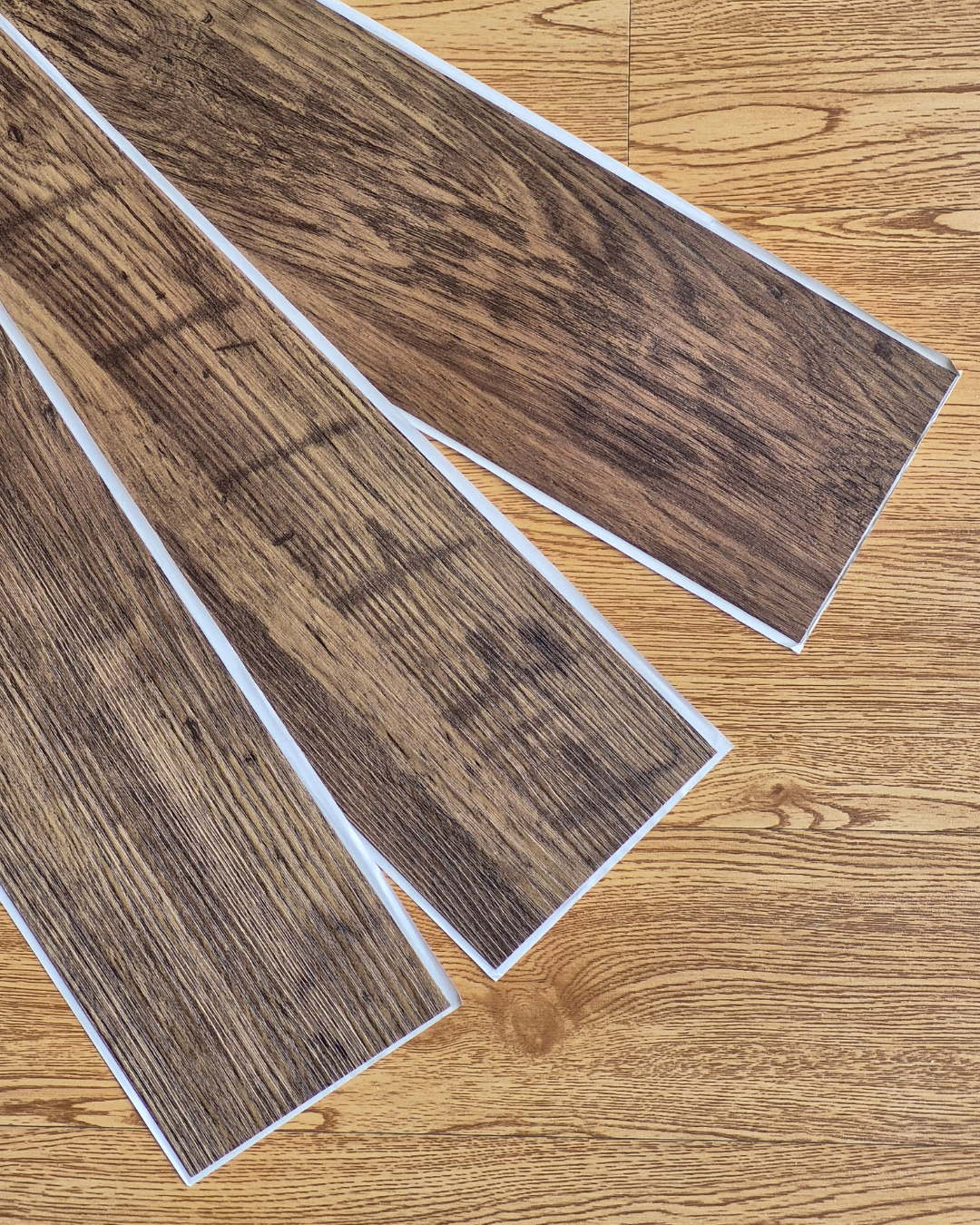 Two pieces of vinyl flooring with a wood grain pattern on a wooden surface.
