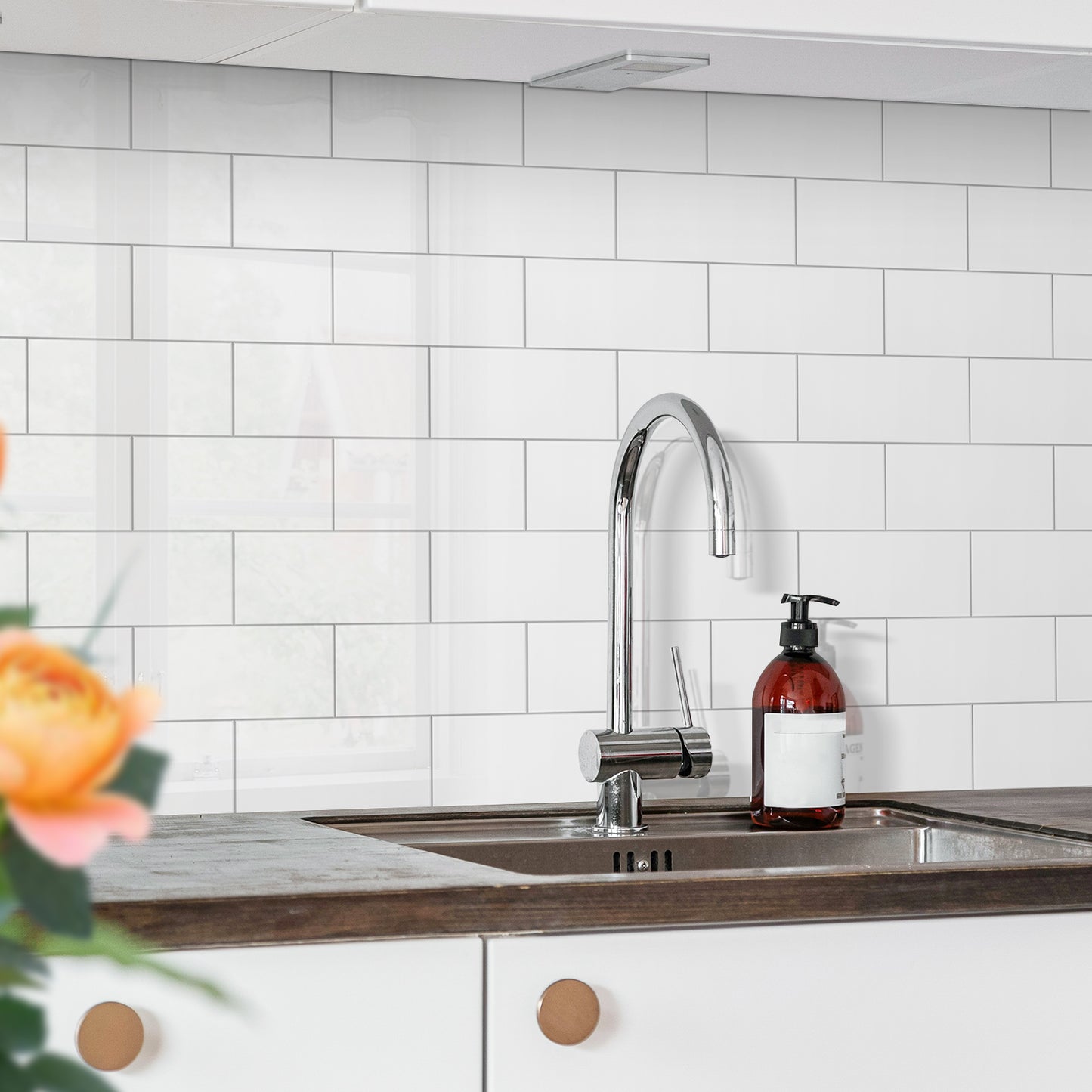 Modern kitchen sink with a faucet and soap dispenser against a white tiled wall.