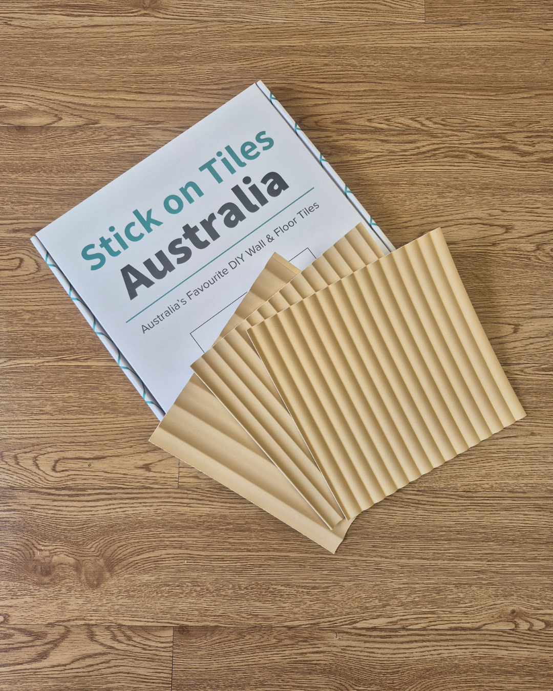 Pack of beige tiles with 'Stick on Tiles Australia' packaging on a wooden floor.
