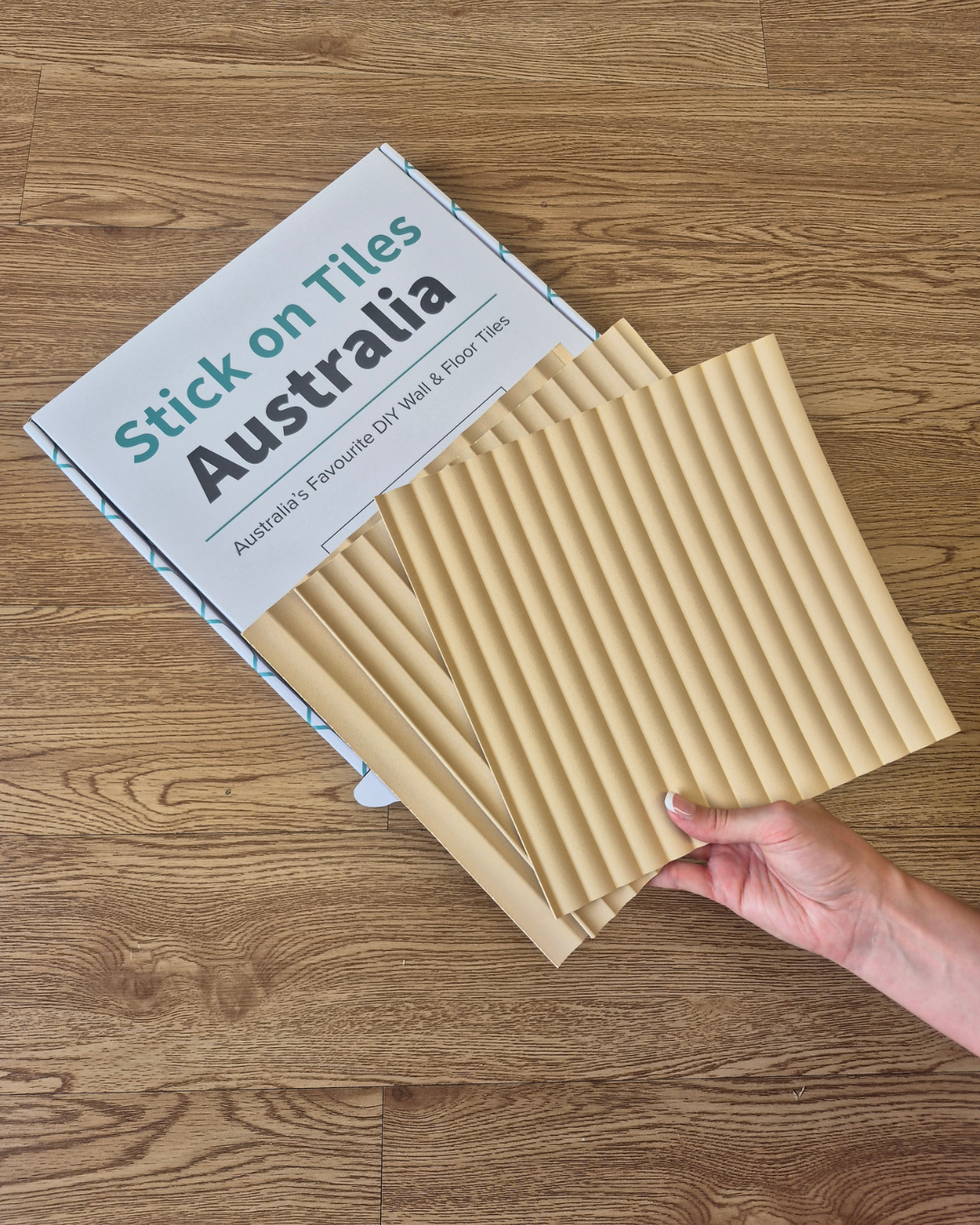 Pack of tiles with 'Stick on Tiles Australia' packaging on a wooden floor.